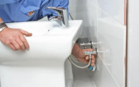 Instalator podłącza wężyki do nowego, białego bidetu.