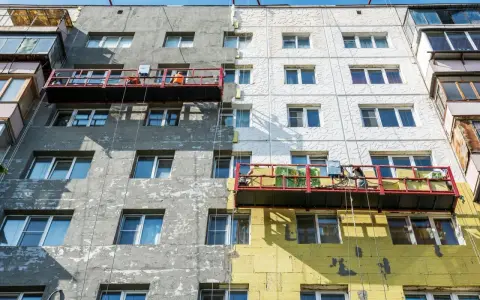 Remont bloku mieszkalnego w toku. Czy remont mieszkania trzeba zgłaszać? Pracownicy na rusztowaniach ocieplają budynek.