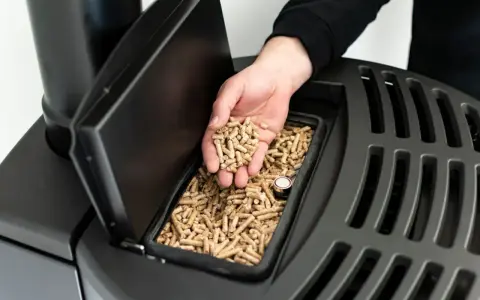 Dłoń wsypuje pellet do zasobnika pieca na pellet i drewno. Opinie o tym modelu są pozytywne.