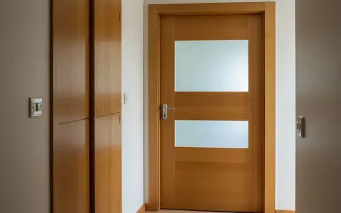 Drewniane drzwi z dwoma przeszkleniami i metalową klamką.