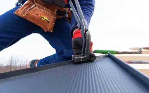 Dekarz pracuje nad dachem, zaginając blachę. To pokazuje, jak obliczyć cenę robocizny dachu za m2.