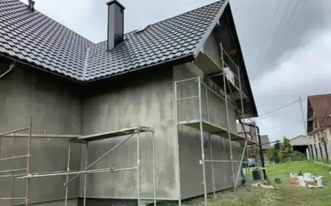 Dom w trakcie ocieplania, rusztowania wokół ścian. Zastanawiasz się, ile kosztuje ocieplenie domu?