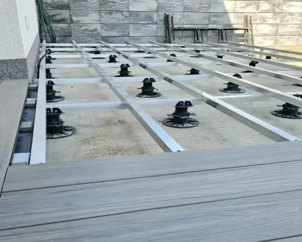Montaż tarasów z deski kompozytowej. Widoczna konstrukcja nośna z aluminiowych profili i regulowanych podpór.