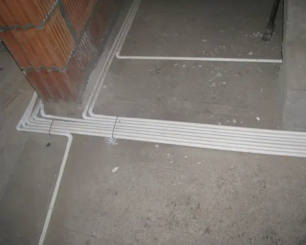 Uporządkowana instalacja elektryczna w podłodze, biegnąca wzdłuż ściany z cegły.