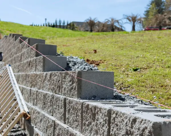 Budowa taniego murku oporowego z bloczków betonowych. Widać drabinę i różową nić traserską.