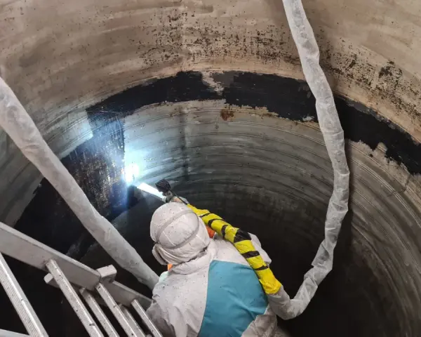 Pracownik w kombinezonie ochronnym wykonuje czyszczenie suchym lodem wnętrza betonowego zbiornika.