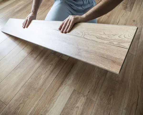 Układanie paneli w kuchni. Dłonie trzymają jasny panel laminowany, który ma imitować drewno.