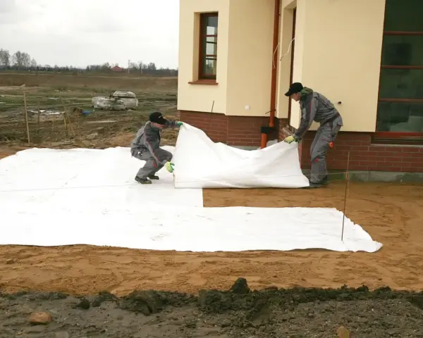 Dwóch robotników rozkłada białą geowłókninę, przygotowując tani taras na gruncie.