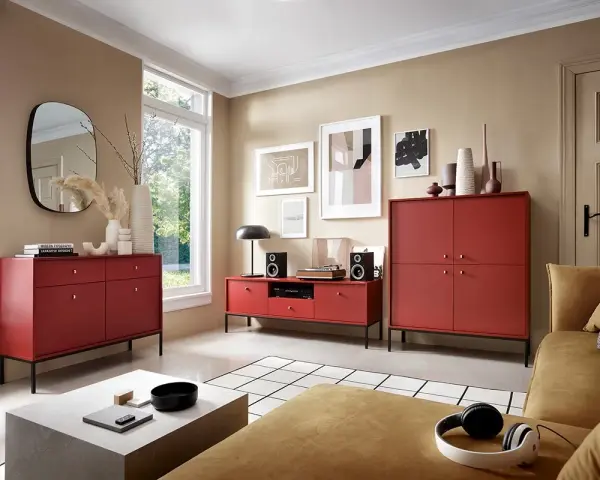 Nowoczesny salon z meblami w kolorze bordowym, w tym szafkami RTV i komodą. Na kanapie leżą słuchawki.