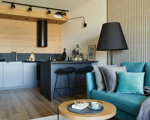 Nowoczesny aneks kuchenny i przytulny salon – inspiracja, jak urządzić mały salon z aneksem. Turkusowa kanapa, drewniane akcenty.