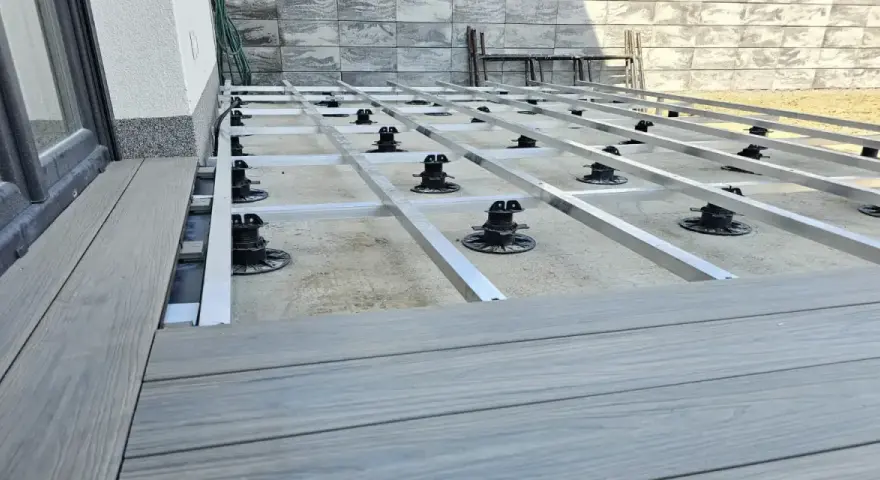 Montaż tarasów z deski kompozytowej. Widoczna konstrukcja nośna z aluminiowych profili i regulowanych podpór.
