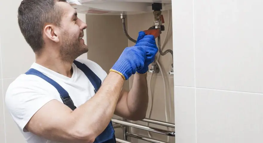 Instalator w niebieskich rękawiczkach dokręca zawór, pokazując, jak spuścić wodę z bojlera.