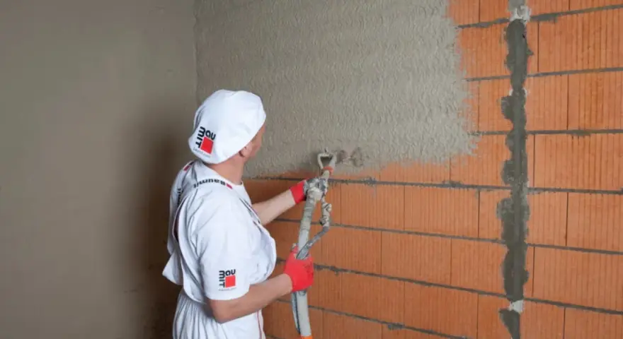 Pracownik nakłada tynk cementowo-wapienny na ścianę z pustaków ceramicznych. Sprawdź atrakcyjną tynki cementowo wapienne cenę!