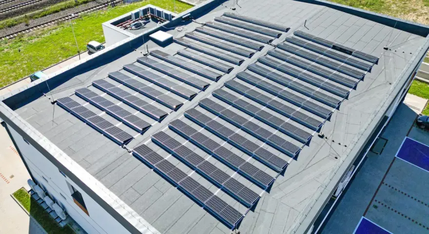 Duży dach płaski pokryty panelami fotowoltaicznymi, które zbierają energię słoneczną.