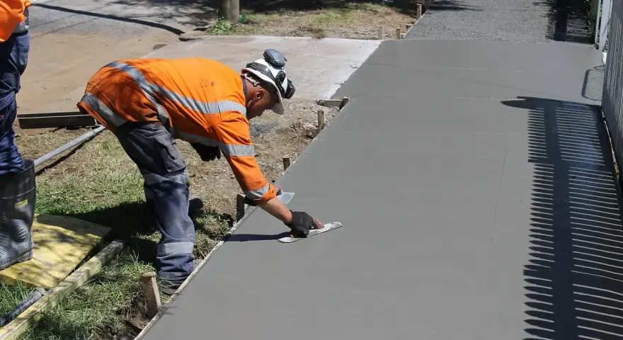 Robotnik w pomarańczowej kamizelce wygładza świeży beton kielnią.