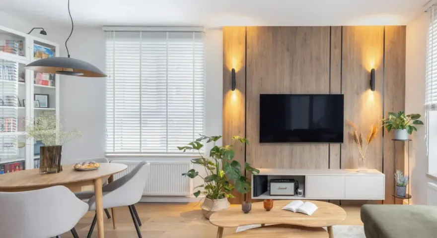 Przytulny salon inspiracje: drewniana ściana z TV, okrągły stół z krzesłami, rośliny i stylowe oświetlenie tworzą ciepłą atmosferę.