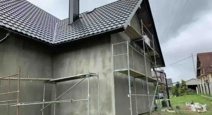Dom w trakcie prac elewacyjnych. Widać rusztowania i świeżo nałożony tynk. Sprawdzamy tynk silikonowy cena za m2 robocizny.