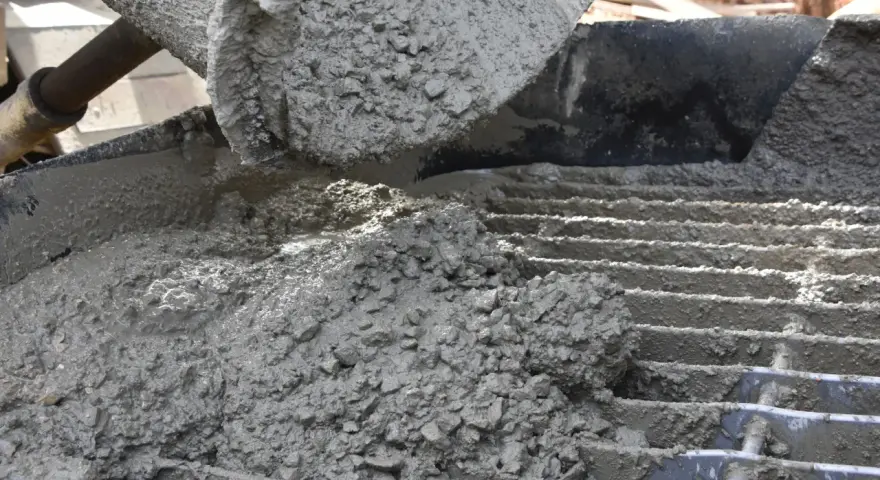 Świeży beton z kruszywem, idealny jako jaki beton pod obrzeża, wylewany z maszyny na ruszt.