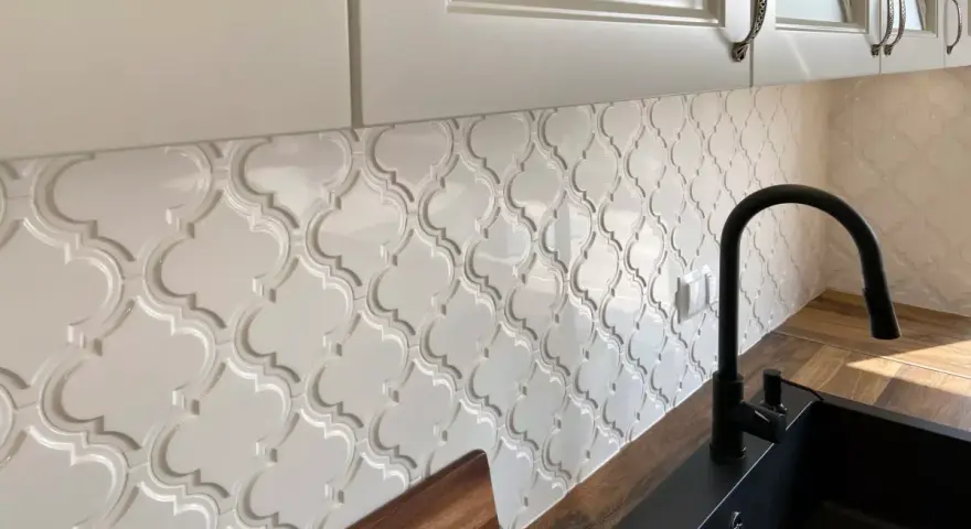 Białe, wypukłe płytki w kształcie arabeski tworzą elegancką mozaikę nad blatem kuchennym.
