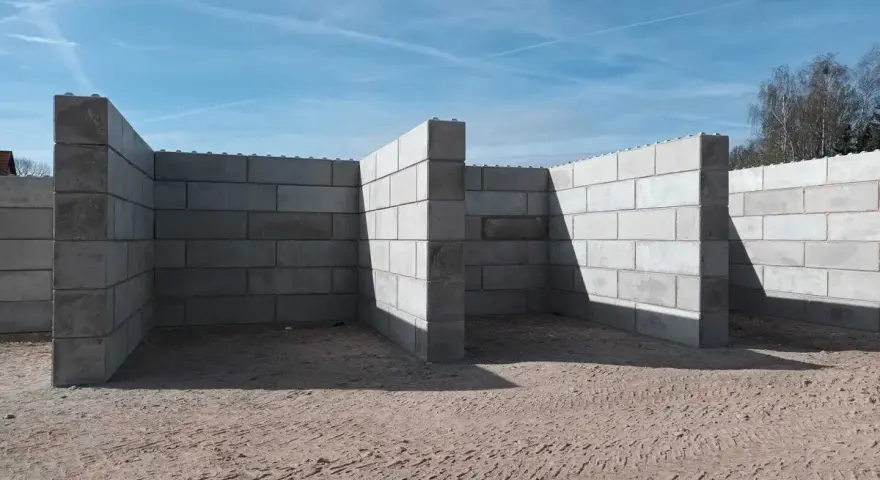 Budowa muru oporowego z betonowych bloczków na piaszczystym podłożu.