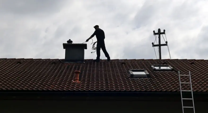 Kominiarz na dachu sprawdza komin. Zastanawiasz się, ile kosztuje przegląd kominiarski?