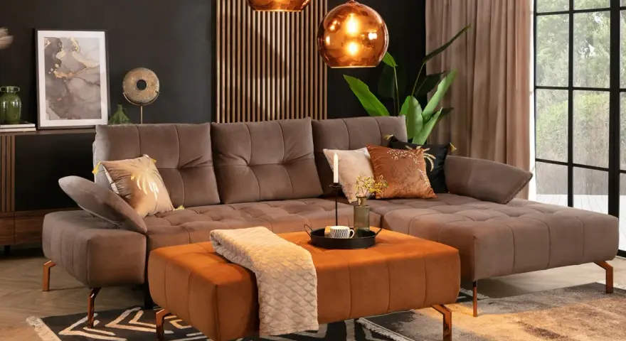 Sofa w kolorze taupe, czyli eleganckim połączeniu brązu i szarości, z pomarańczową pufą i miedzianymi dodatkami.