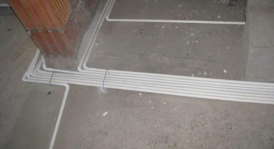 Uporządkowana instalacja elektryczna w podłodze, biegnąca wzdłuż ściany z cegły.