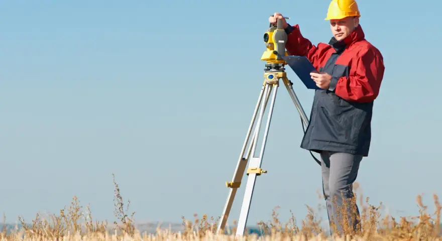 Geodeta w żółtym kasku pracuje z tachimetrem na polu. Zastanawiasz się, ile kosztuje geodeta?