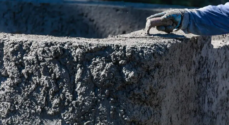 Dłoń w rękawicy wygładza mokry beton na budowie.