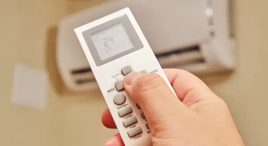 Dłoń trzymająca pilot do klimatyzatora, ustawiająca temperaturę 24°C. Ogrzewanie klimatyzatorem zapewnia komfort.