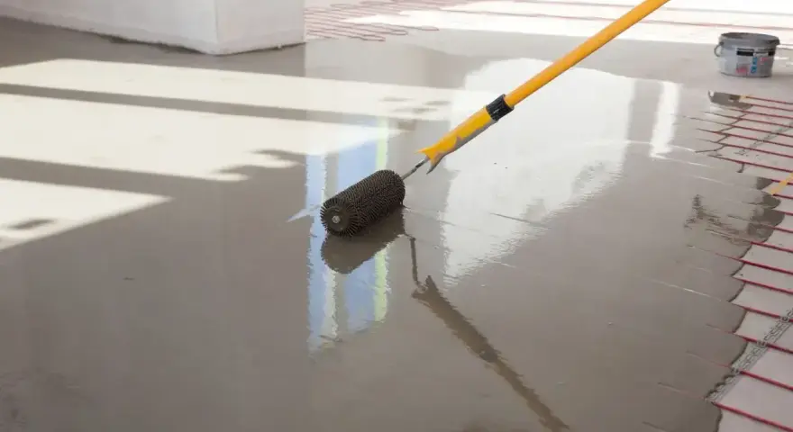 Wałek do betonu wygładzający świeżą wylewkę na podłodze z ogrzewaniem podłogowym.