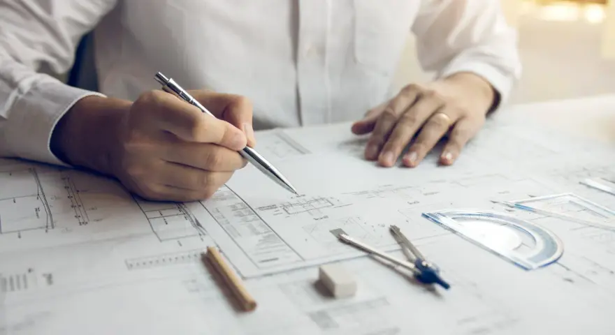 Inżynier z uprawnieniami budowlanymi elektrycznymi analizuje projekt, trzymając długopis nad dokumentacją techniczną.
