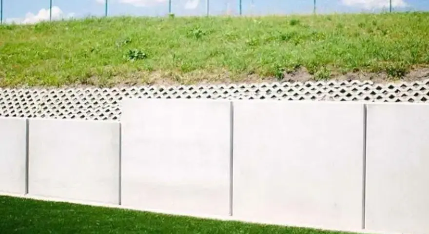 Betonowy mur oporowy z ażurową warstwą i zieloną skarpą.
