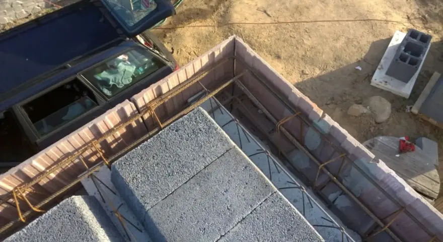 Budowa stropu ackermana w toku. Betonowe pustaki i zbrojenie czekają na zalanie betonem. Obok stoi samochód.