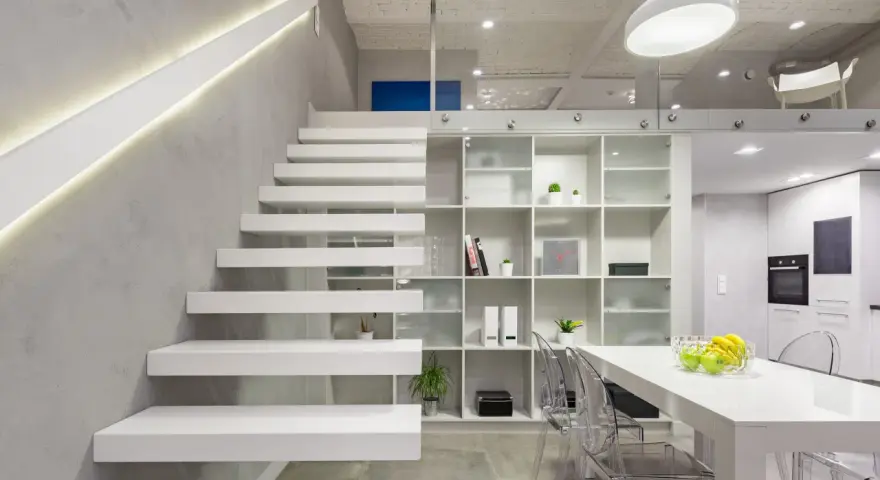 Nowoczesna antresola z białymi, lewitującymi schodami, przeszklonymi balustradami i minimalistycznym regałem.