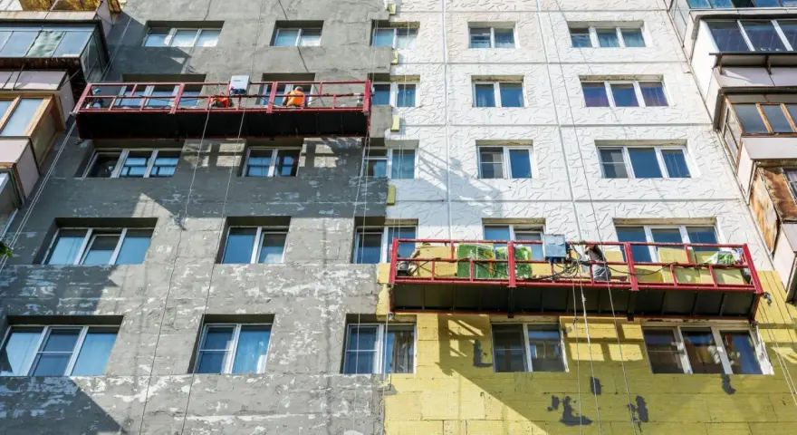 Remont bloku mieszkalnego w toku. Czy remont mieszkania trzeba zgłaszać? Pracownicy na rusztowaniach ocieplają budynek.
