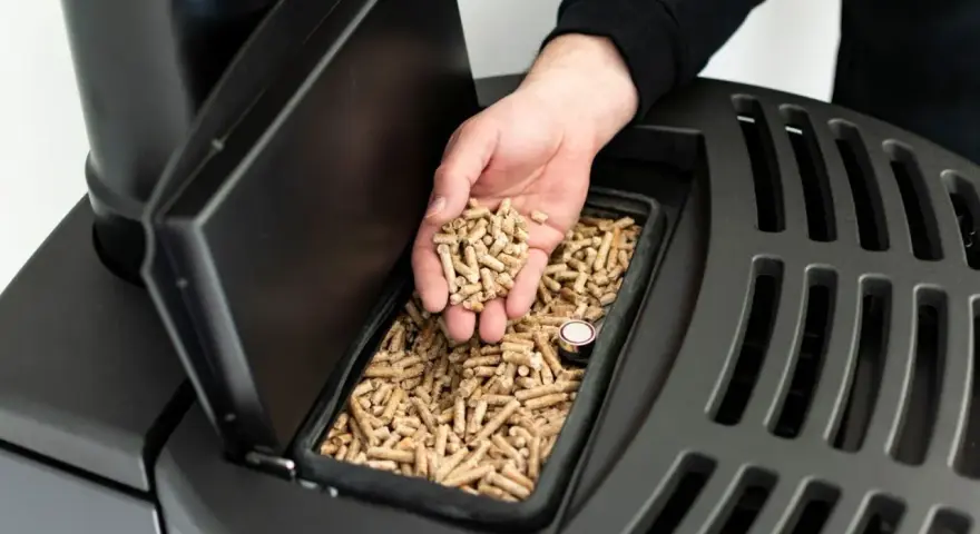 Dłoń wsypuje pellet do zasobnika pieca na pellet i drewno. Opinie o tym modelu są pozytywne.