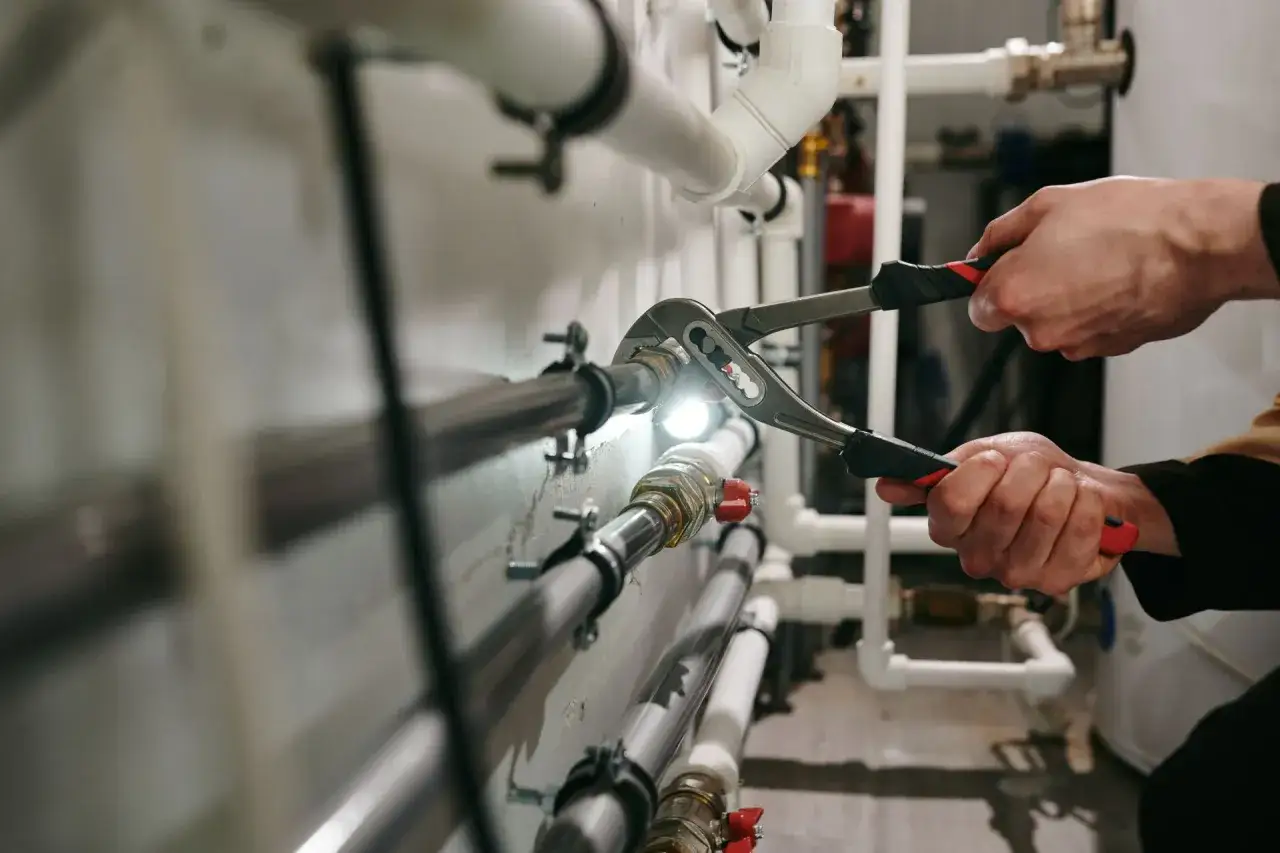 Ręce hydraulika dokręcają złączkę kluczem. Biały montaż instalacji wodnej w trakcie prac.