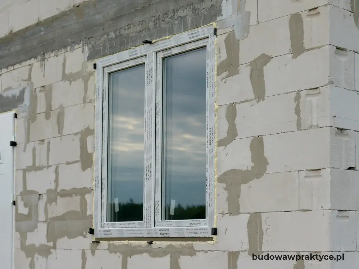 Okna w bloku z betonu komórkowego, z widocznym nadprożem i pianką montażową. Budowa w toku.
