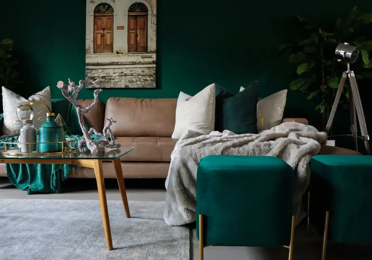 Elegancki salon z brązową kanapą, poduszkami w odcieniach zieleni i złota, puszystym kocem oraz pufami w intensywnym, seledynowym kolorze.