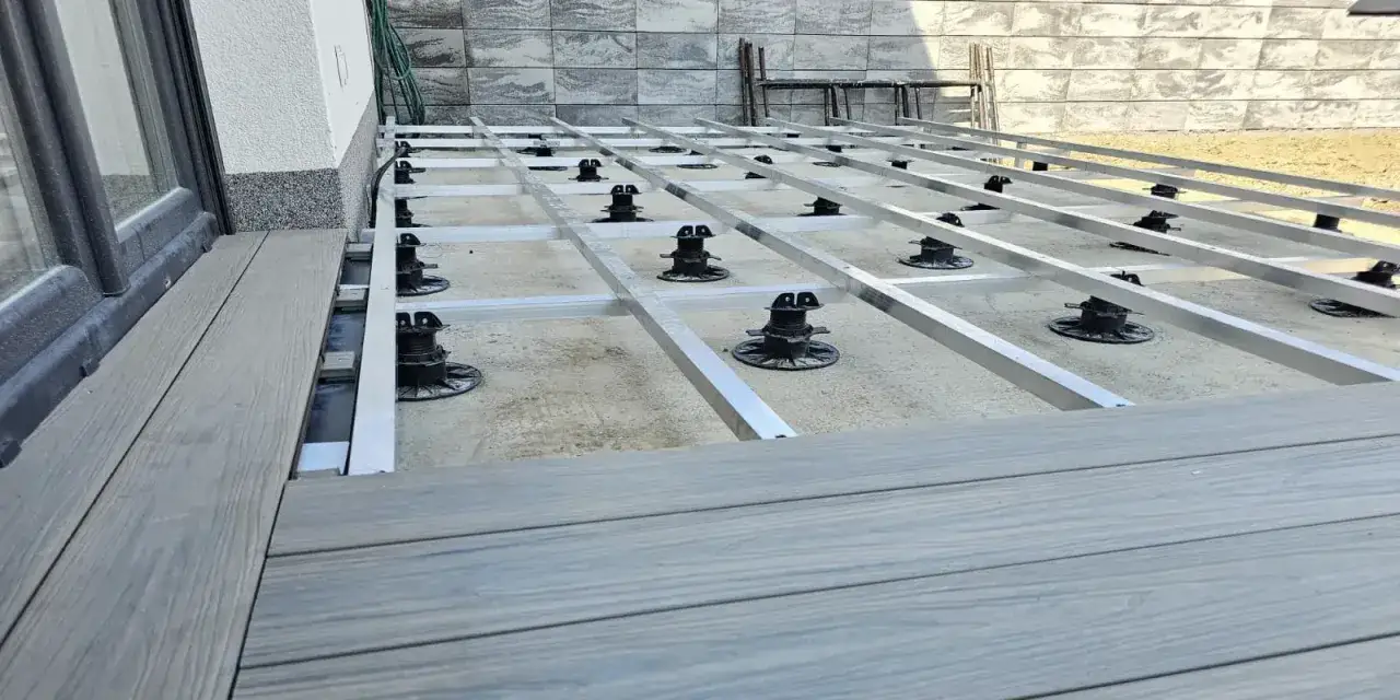 Montaż tarasów z deski kompozytowej. Widoczna konstrukcja nośna z aluminiowych profili i regulowanych podpór.