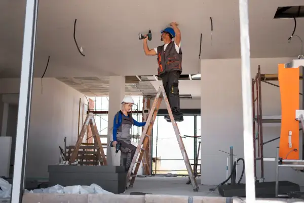 Dwóch budowlańców na drabinach montuje instalację elektryczną. Czy jest ulga na remont mieszkania?